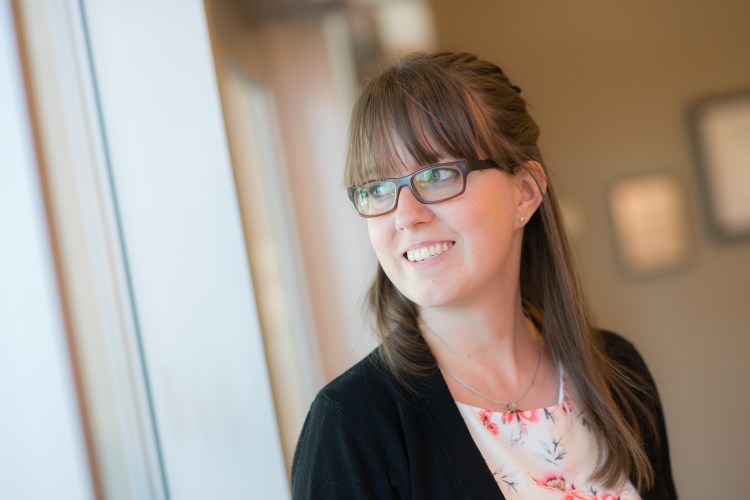 Jenn is in a professional setting looking out a window to her left.