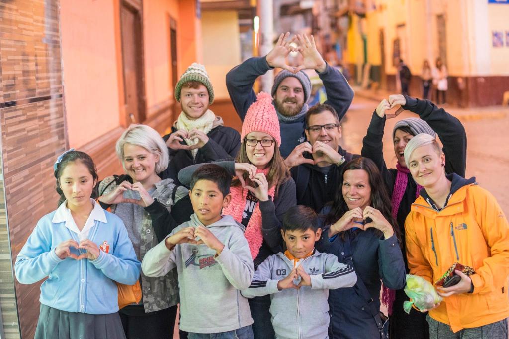 Jenn Is standing with a group of adults and children making heart shapes with their hands